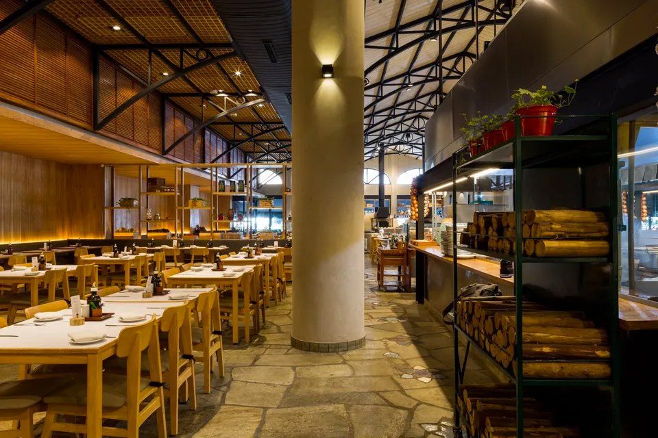 Um restaurante com mesas e cadeiras e uma cozinha ao fundo.