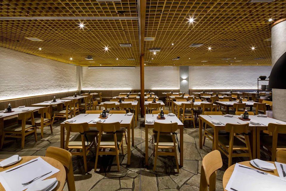 Um restaurante com mesas e cadeiras e teto de madeira.