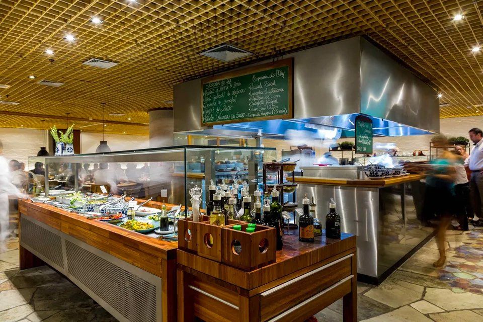 Um restaurante com fila de buffet e uma cozinha ao fundo.
