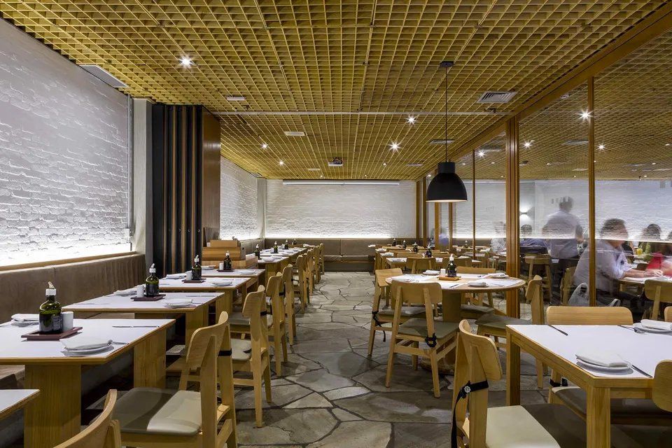 Um restaurante com mesas e cadeiras e um homem parado ao fundo.