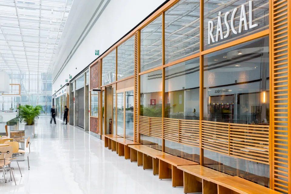 Um restaurante em um shopping com muitas vitrines e bancos de madeira.