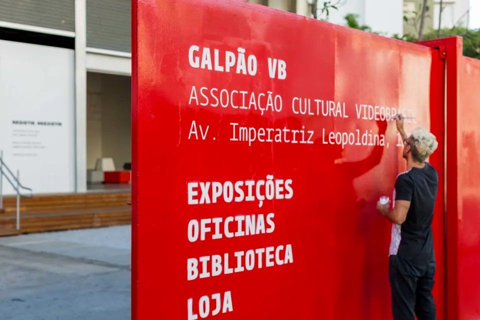 Um homem está escrevendo em uma placa vermelha que diz galpão vb