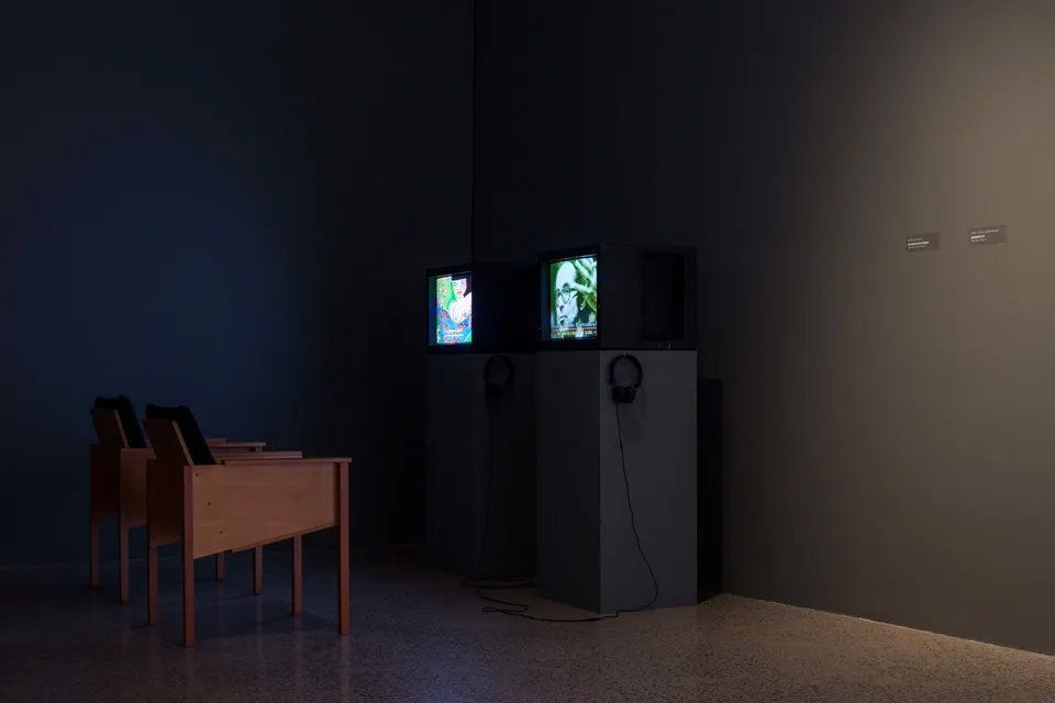 Uma sala escura com duas cadeiras e três televisões.