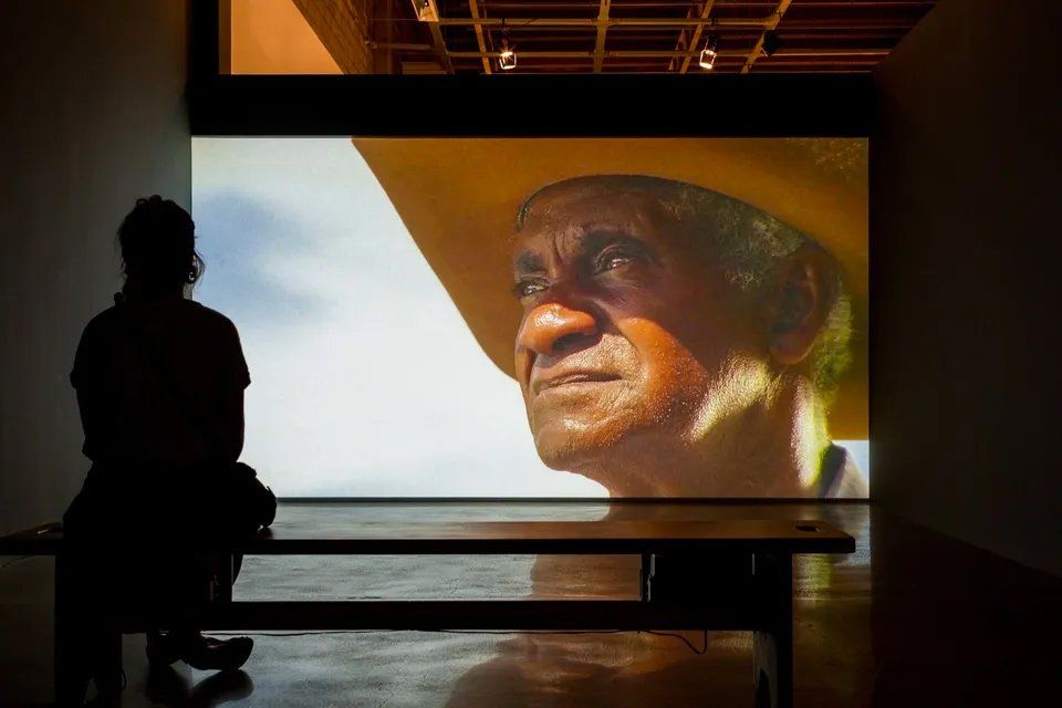 Um homem está sentado em um banco em frente a uma tela grande.
