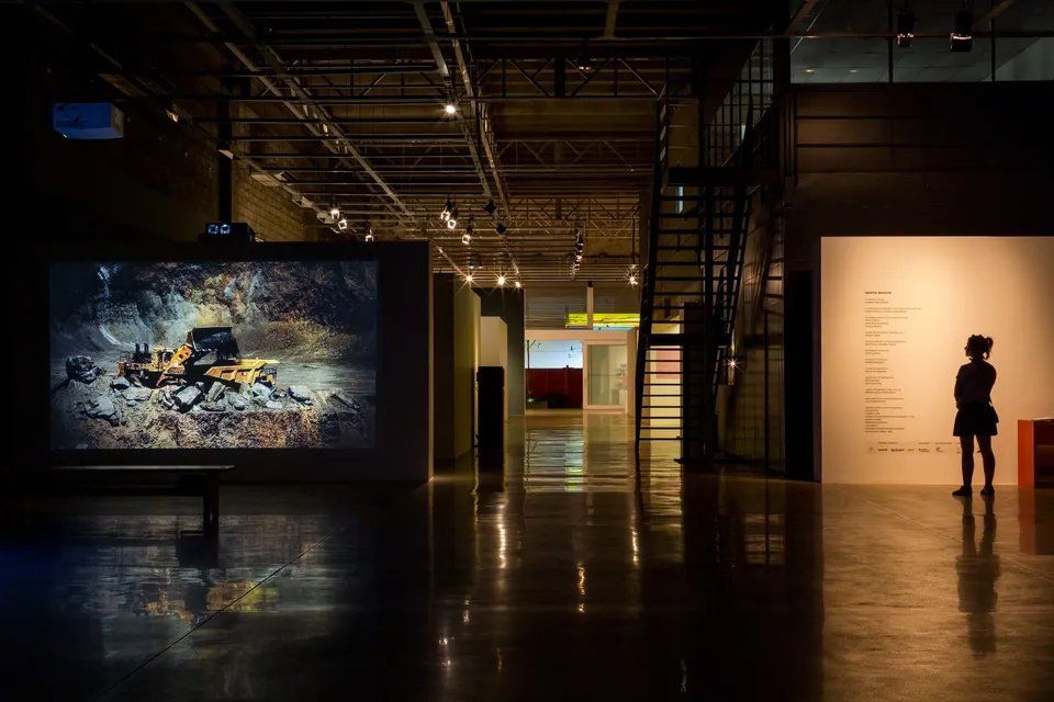 Uma mulher está diante de uma grande tela em um quarto escuro.