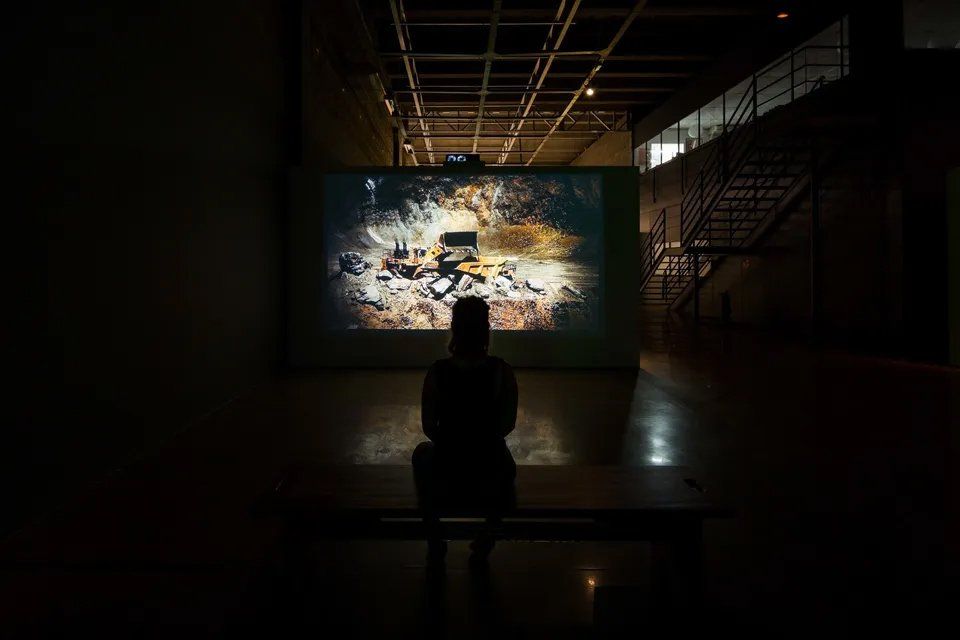 Uma mulher está sentada em frente a uma tela grande em um quarto escuro.