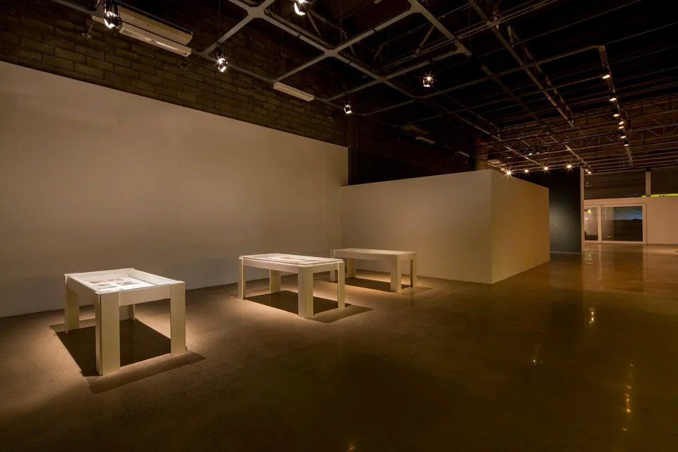 Três mesas brancas estão sentadas em uma grande sala vazia.