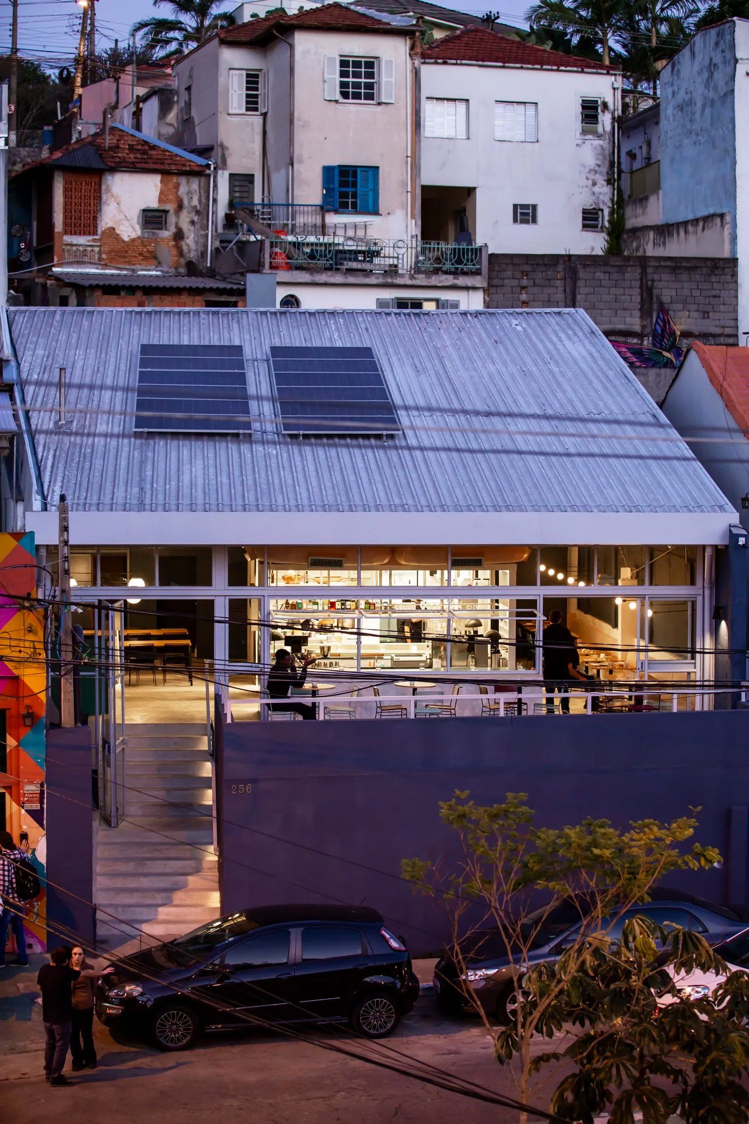 Um carro está estacionado em frente a um prédio com painéis solares no telhado.