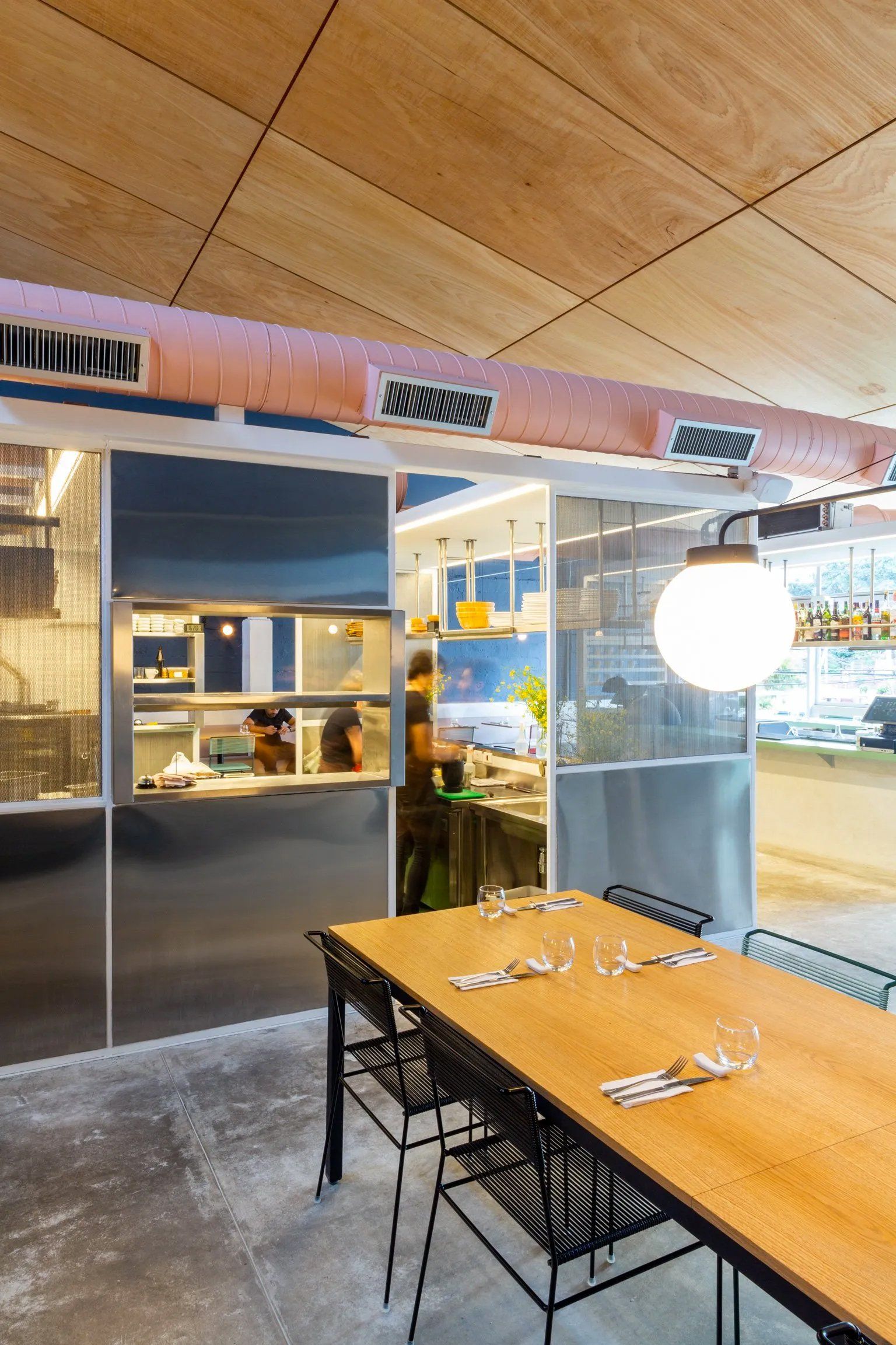 Um restaurante com uma longa mesa e cadeiras em frente a uma cozinha.