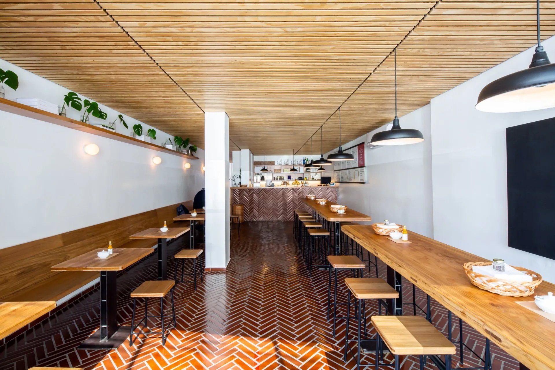 Um restaurante com mesas e bancos de madeira e piso de tijolos.