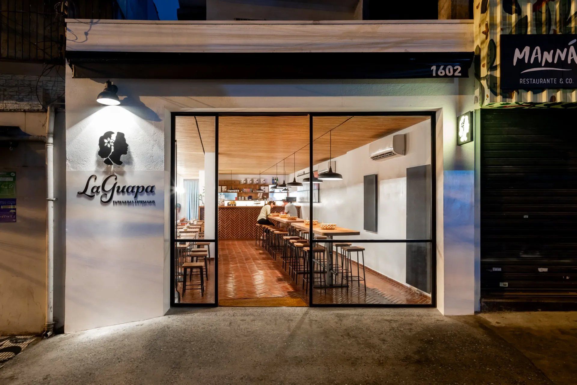 A frente de um restaurante com mesas e cadeiras e uma grande porta de vidro.