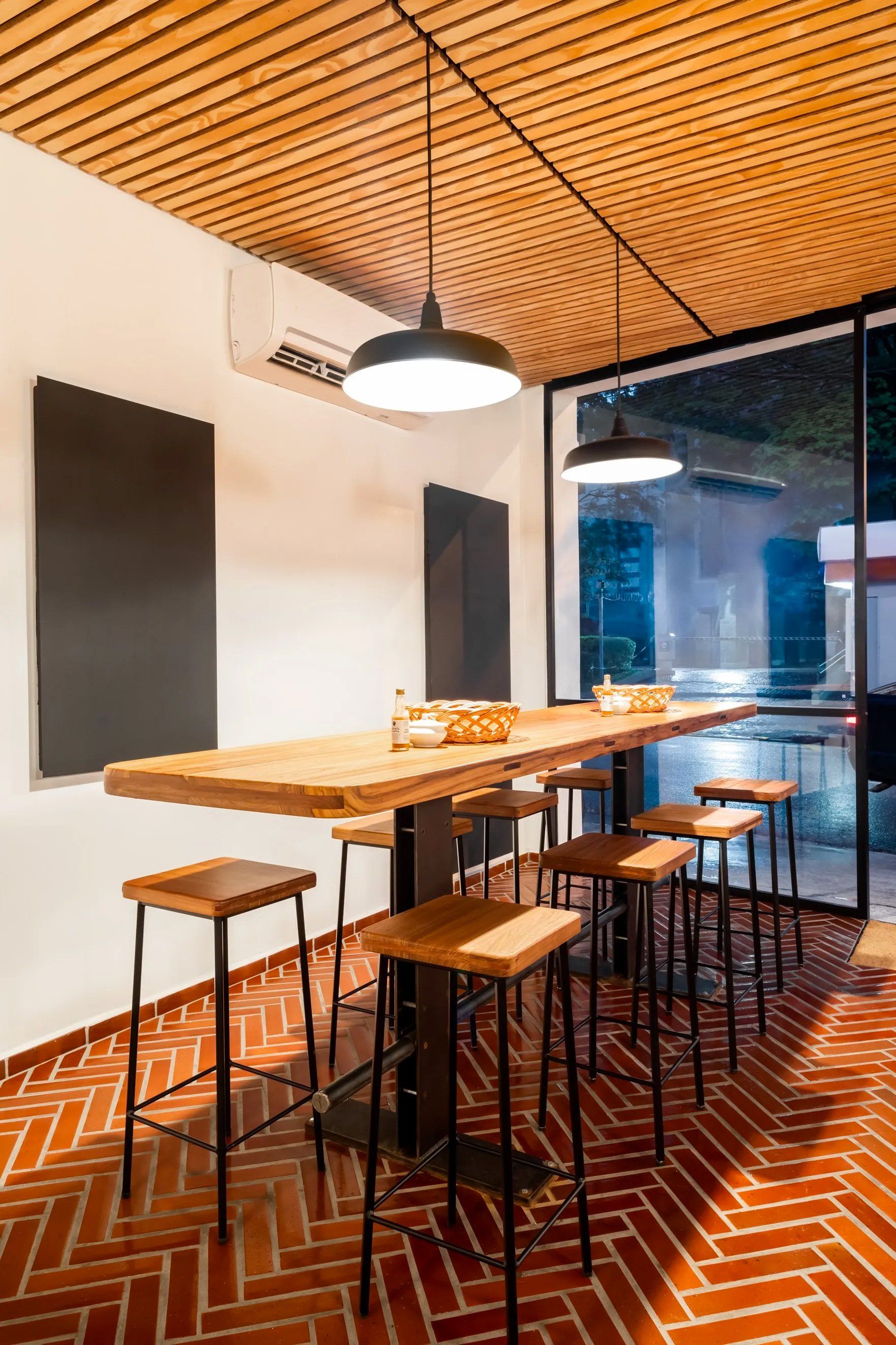 Uma longa mesa de madeira com bancos em uma sala com piso de tijolos.