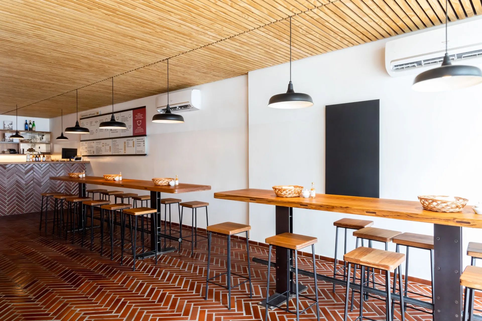 Um restaurante com mesas e bancos e teto de madeira.