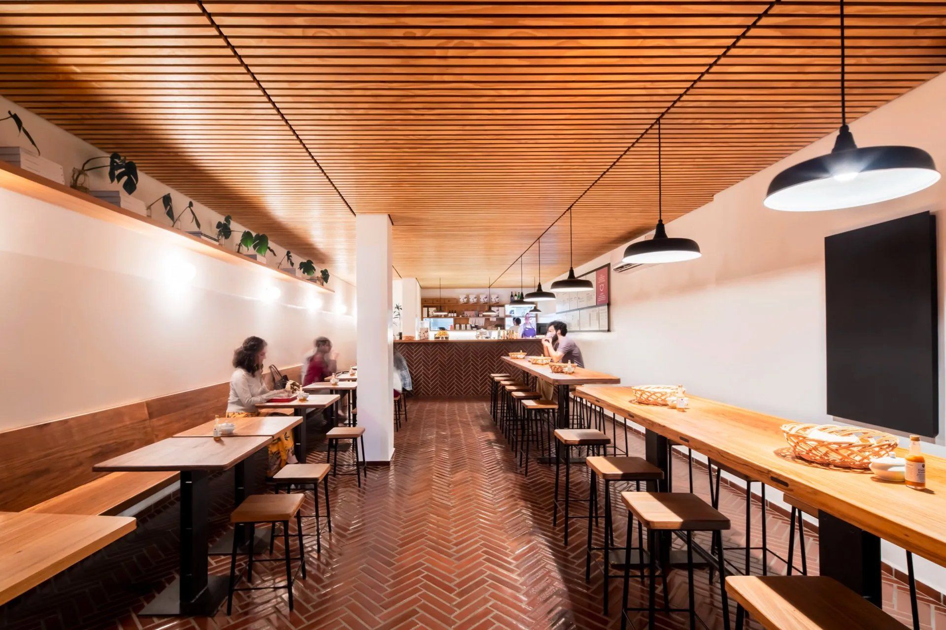 Um restaurante com mesas e bancos e teto de madeira.