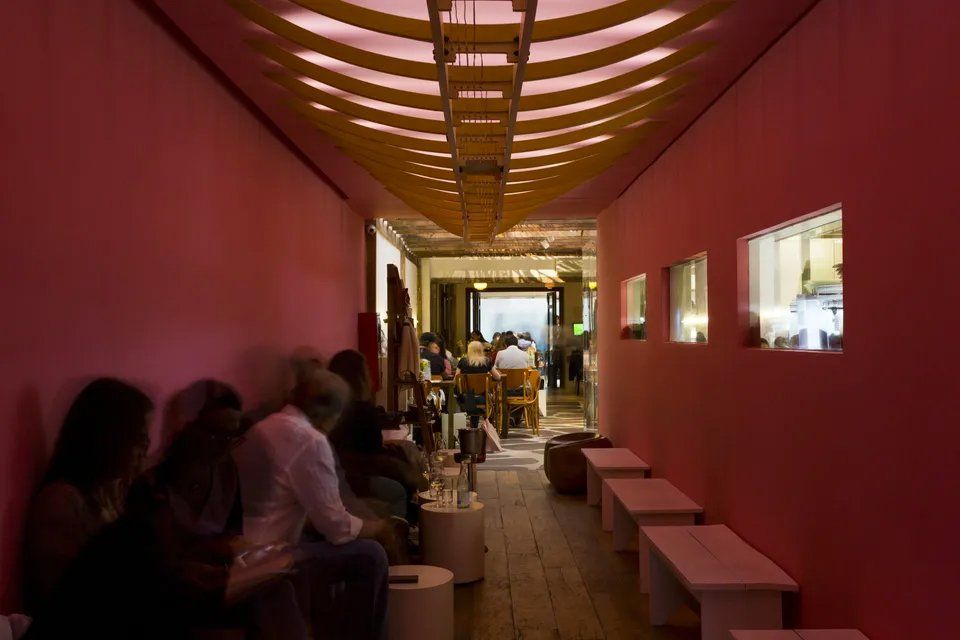 Um grupo de pessoas está sentado em um longo corredor com paredes rosa.