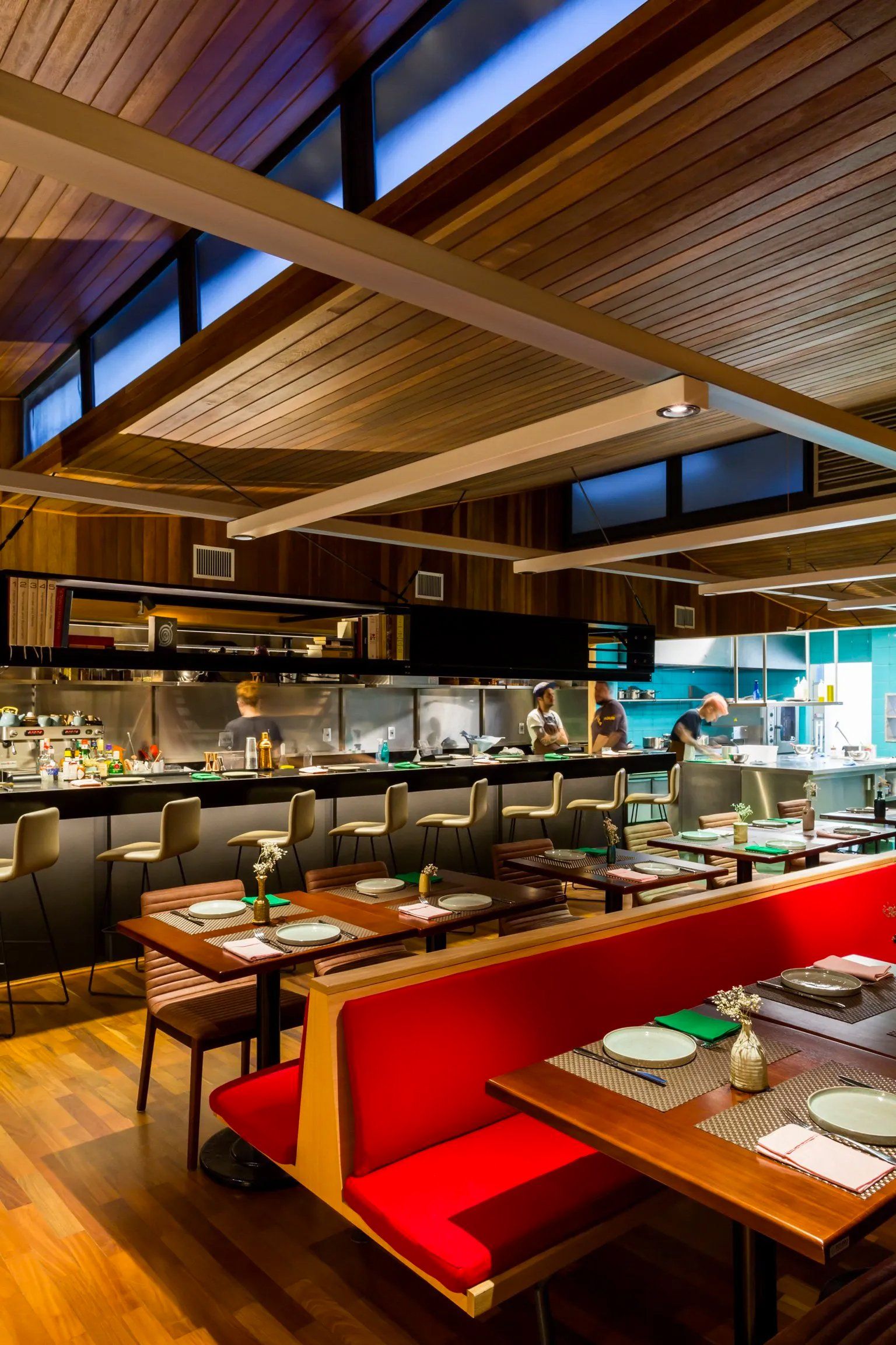 Um restaurante com mesas e bancos e uma cozinha ao fundo