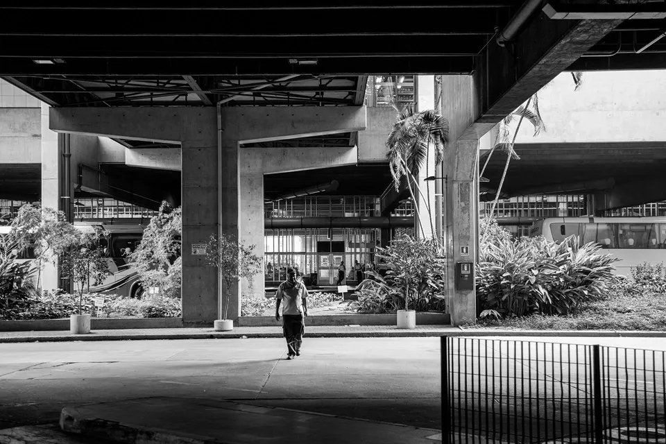 Uma foto em preto e branco de uma pessoa andando sob uma ponte.