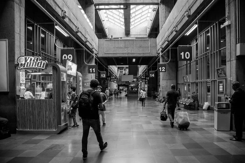 Uma foto em preto e branco de pessoas caminhando por um terminal de aeroporto.