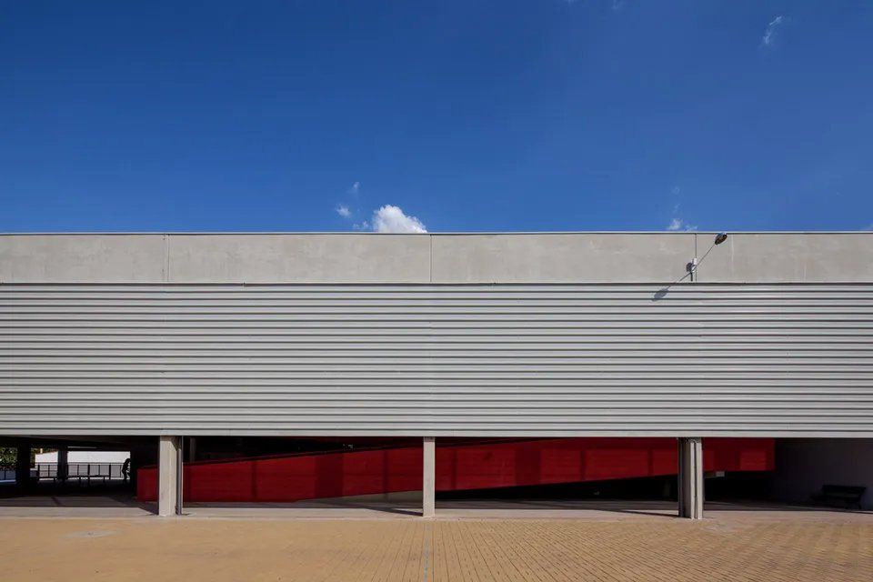 Um grande edifício com uma porta vermelha e um céu azul ao fundo.