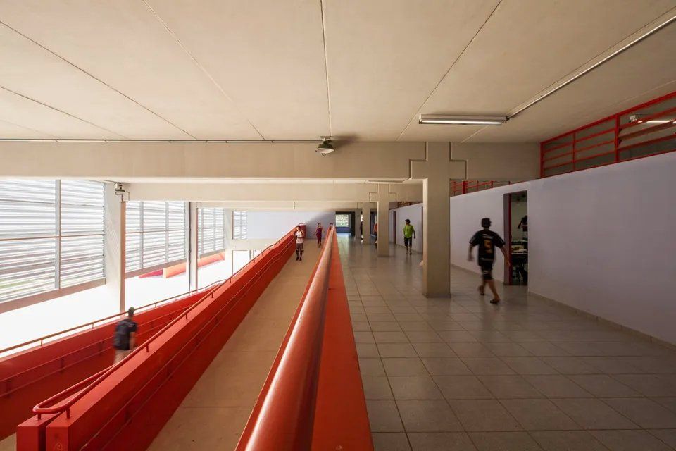 Um longo corredor com uma grade vermelha e pessoas andando por ele.