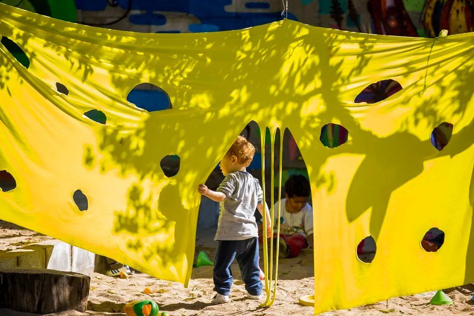 Um menino está diante de um grande pano amarelo com buracos.
