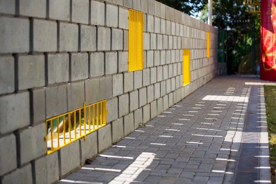 Uma parede de tijolos com janelas amarelas e uma calçada na frente.