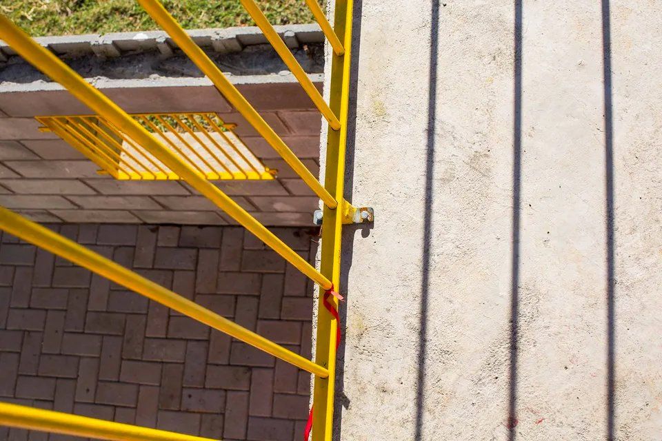 Uma cerca de metal amarela cerca uma passarela de tijolos.