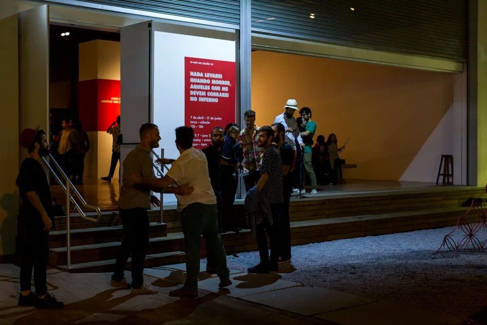 Um grupo de pessoas está do lado de fora de um prédio à noite.