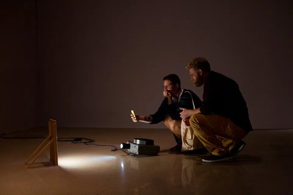 Dois homens estão ajoelhados em uma sala escura olhando para um projetor.