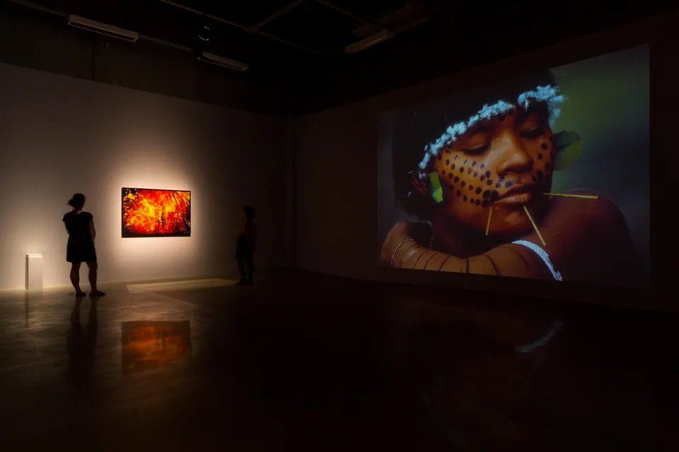 Uma mulher está diante de uma tela grande com a foto de uma mulher.