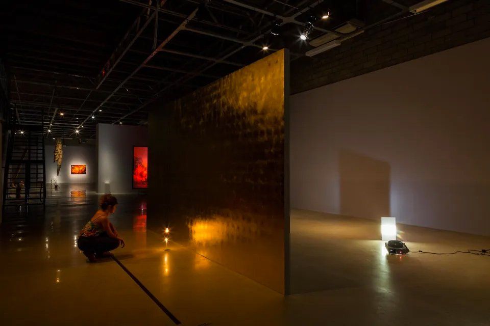 Uma mulher está ajoelhada em um quarto escuro olhando para uma pintura.