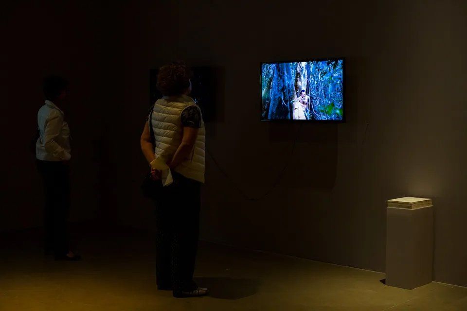 Uma mulher está diante de uma televisão em um quarto escuro.