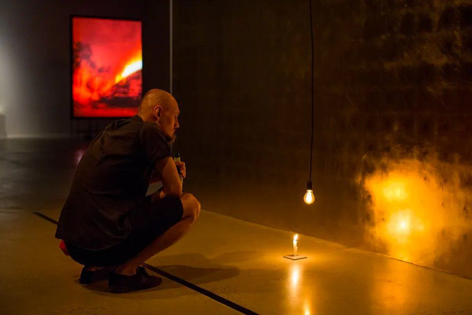 Um homem está ajoelhado diante de uma vela em um quarto escuro.