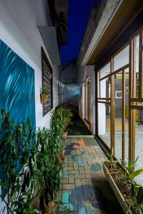 Um corredor estreito entre dois prédios com plantas e uma pintura na parede.