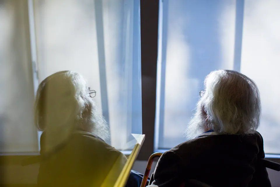 Um homem idoso em uma cadeira de rodas está olhando pela janela.