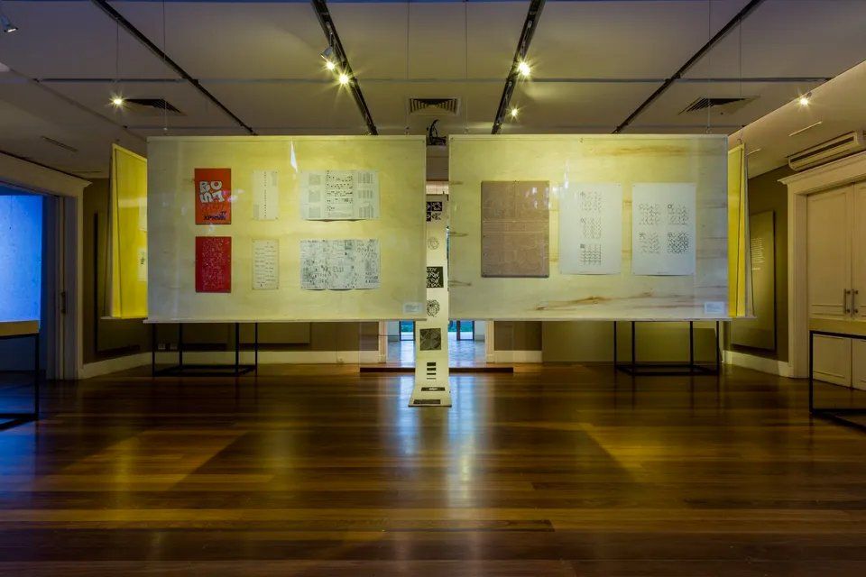 Uma sala ampla com piso de madeira e uma exposição de pinturas na parede.