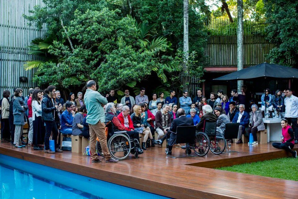 Um grupo de pessoas em cadeiras de rodas está sentado em um deck próximo a uma piscina.