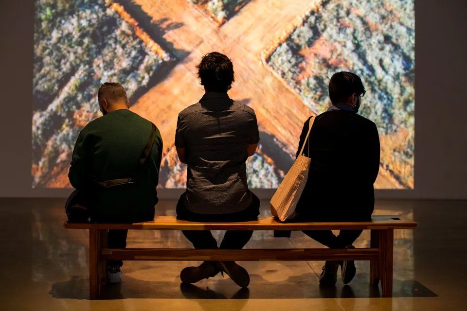 Três pessoas estão sentadas em um banco em frente a uma tela de projetor.