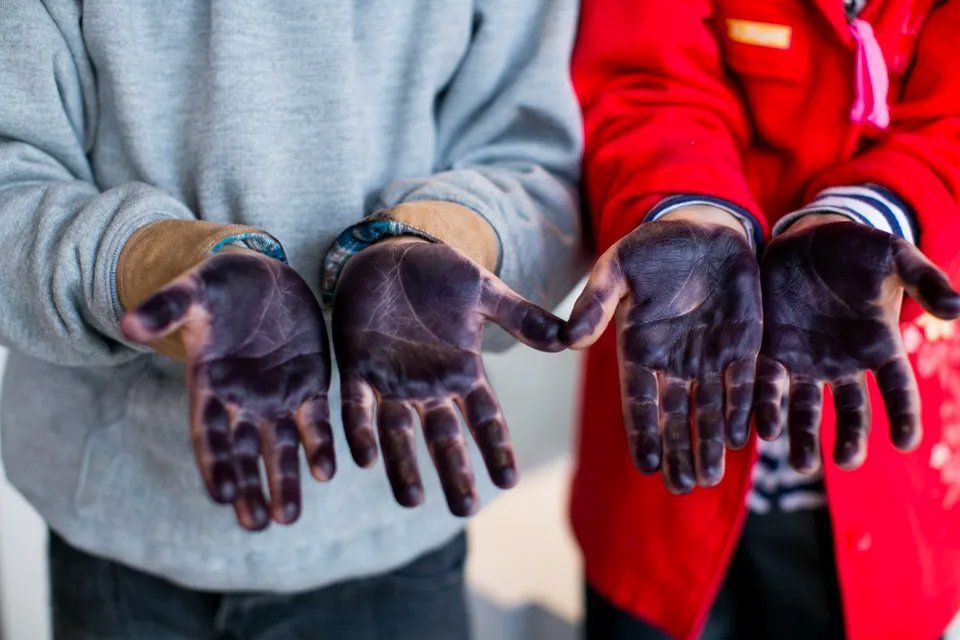 Duas pessoas estão com as mãos cobertas de tinta roxa.