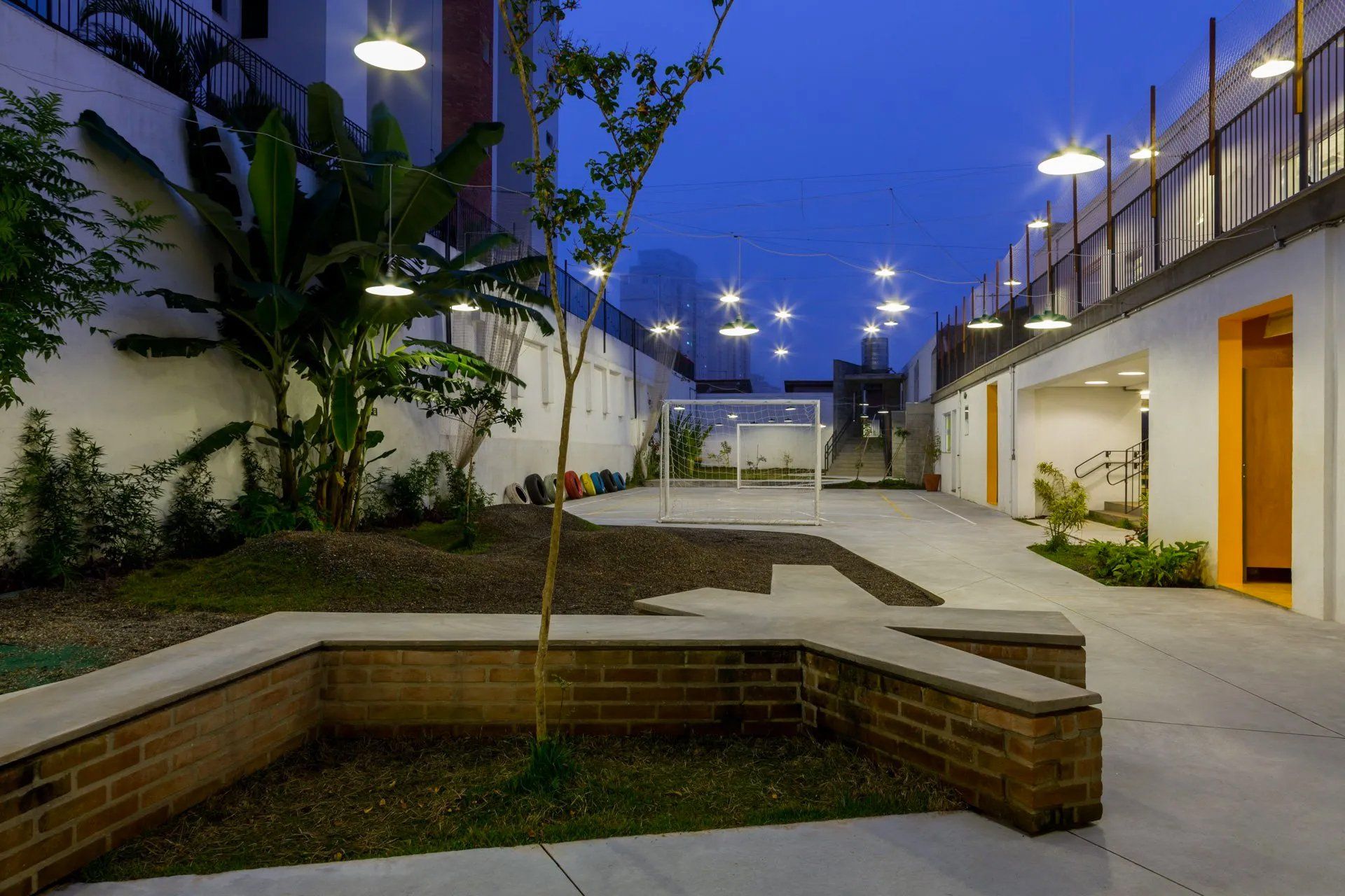 Um pátio com parede de tijolos e um gol de futebol à noite.