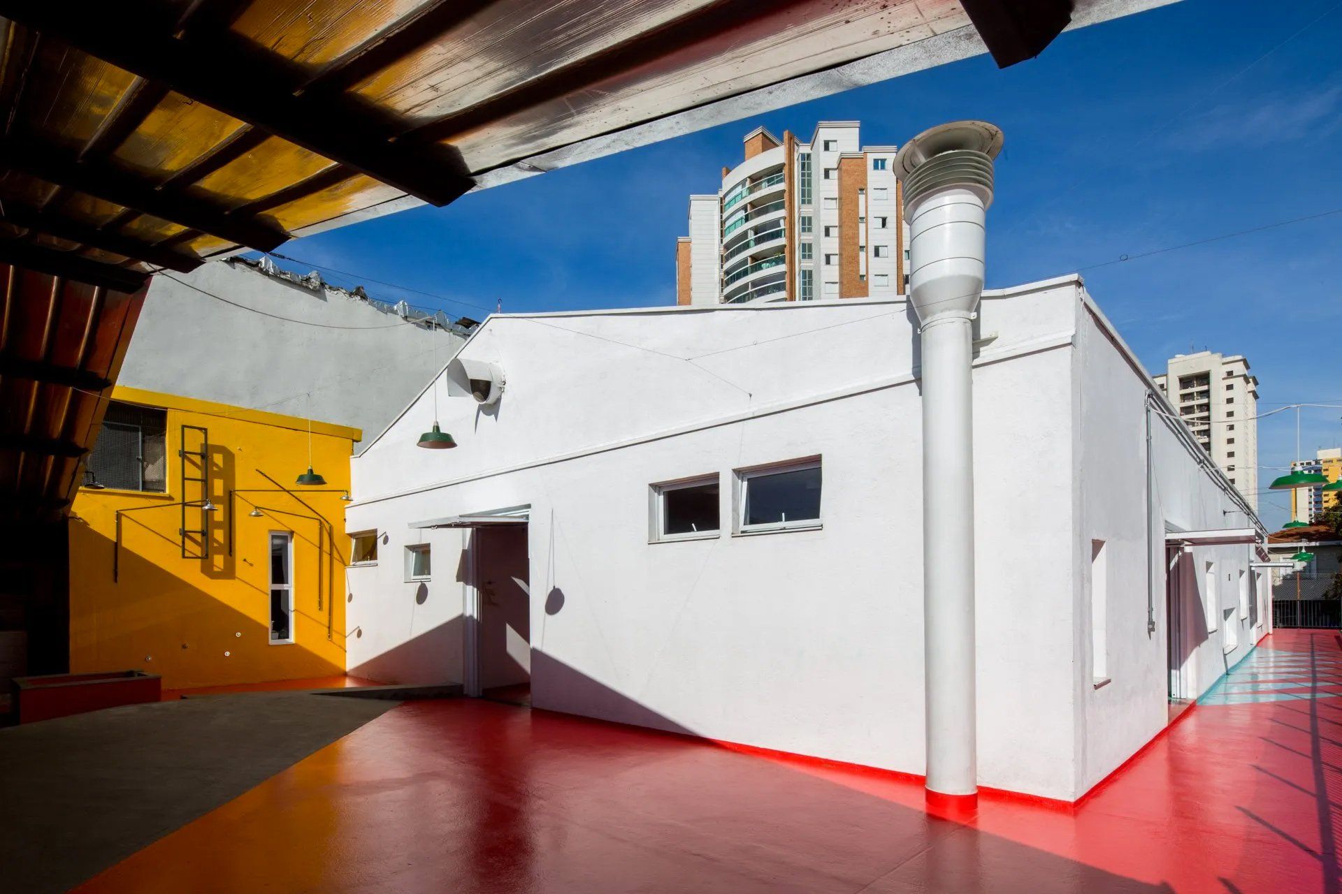 Um prédio branco com piso vermelho e um prédio amarelo ao fundo