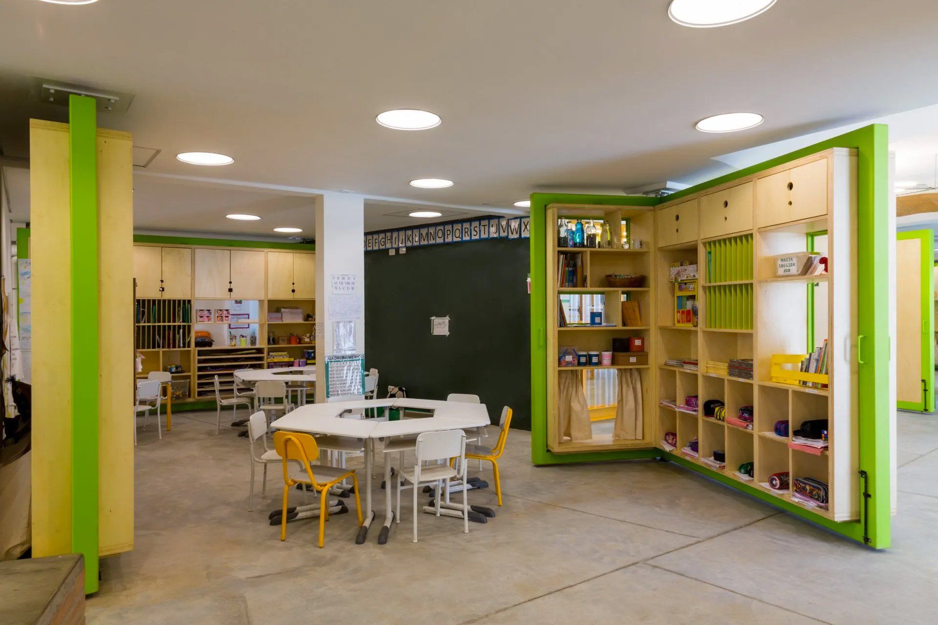 Uma sala de aula com mesas e cadeiras e uma parede verde.