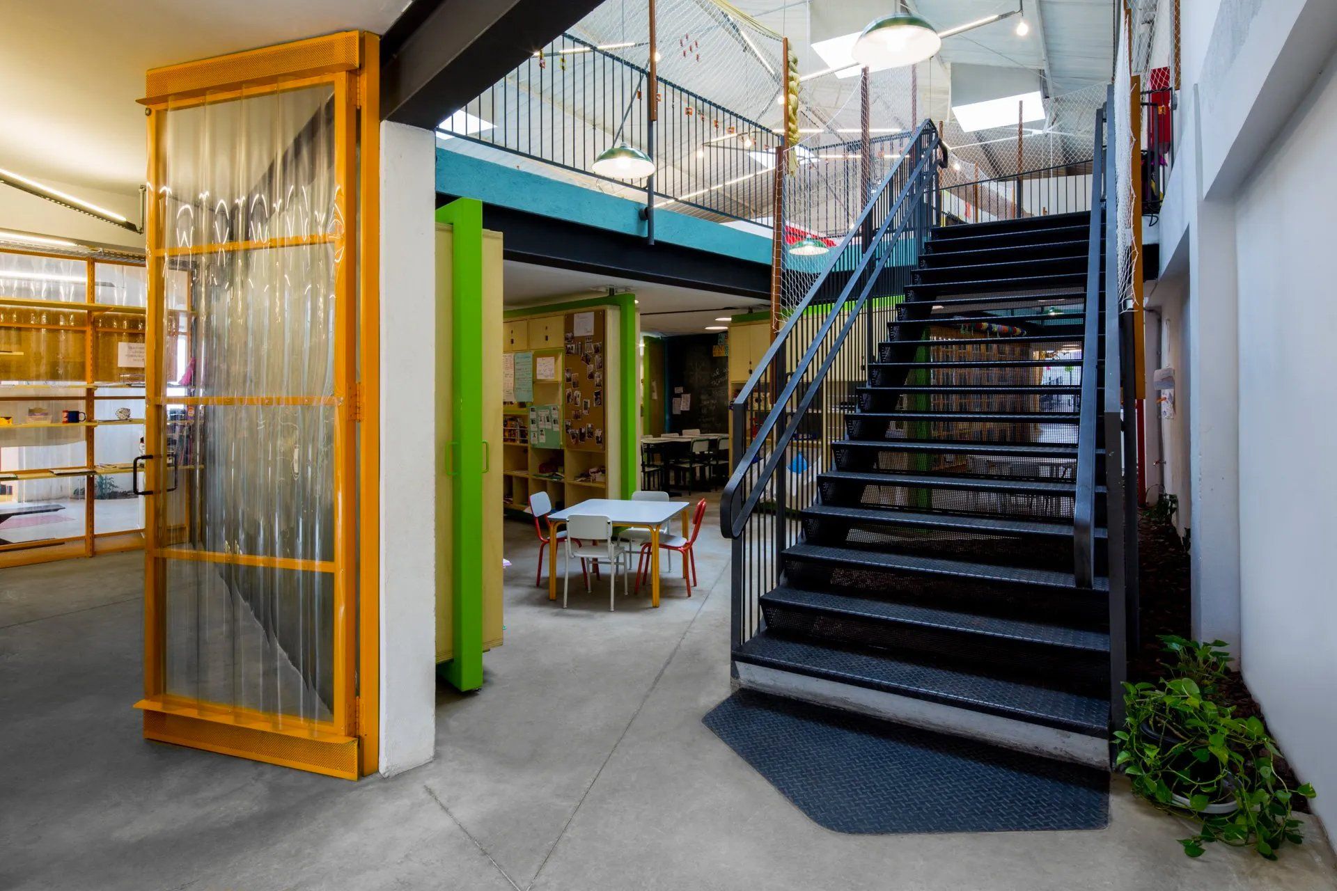 Uma sala com escadas que levam ao segundo andar e mesa e cadeiras.