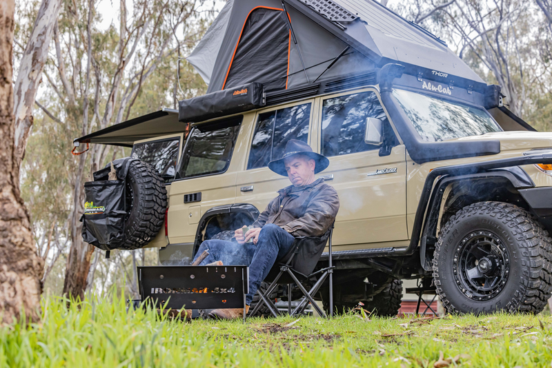 A man is sitting in a chair in front of a jeep with a tent on top of it.