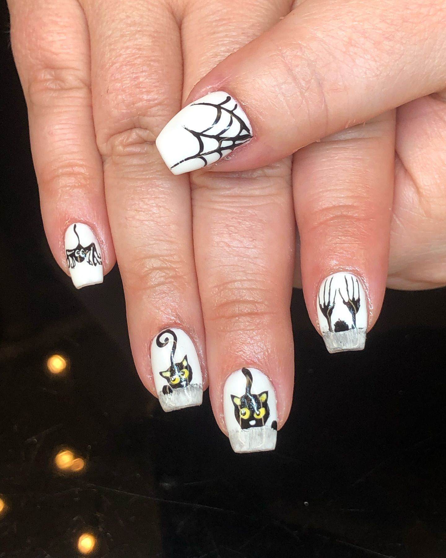 A woman 's nails are decorated with spider webs and black cats
