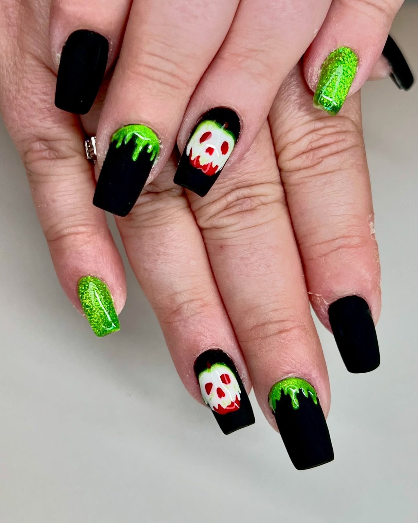 A woman 's nails are painted black and green with a skull on them.