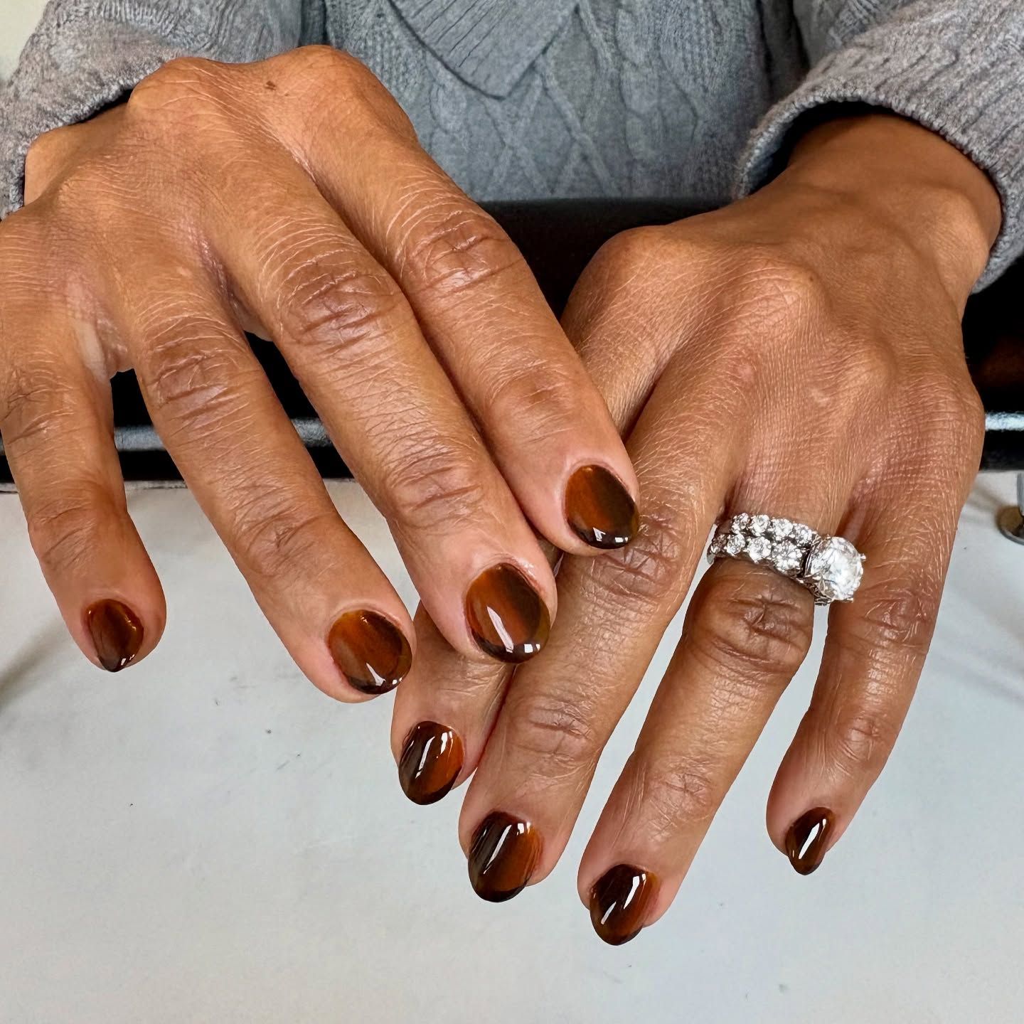 A woman 's hands with brown nails and a diamond ring