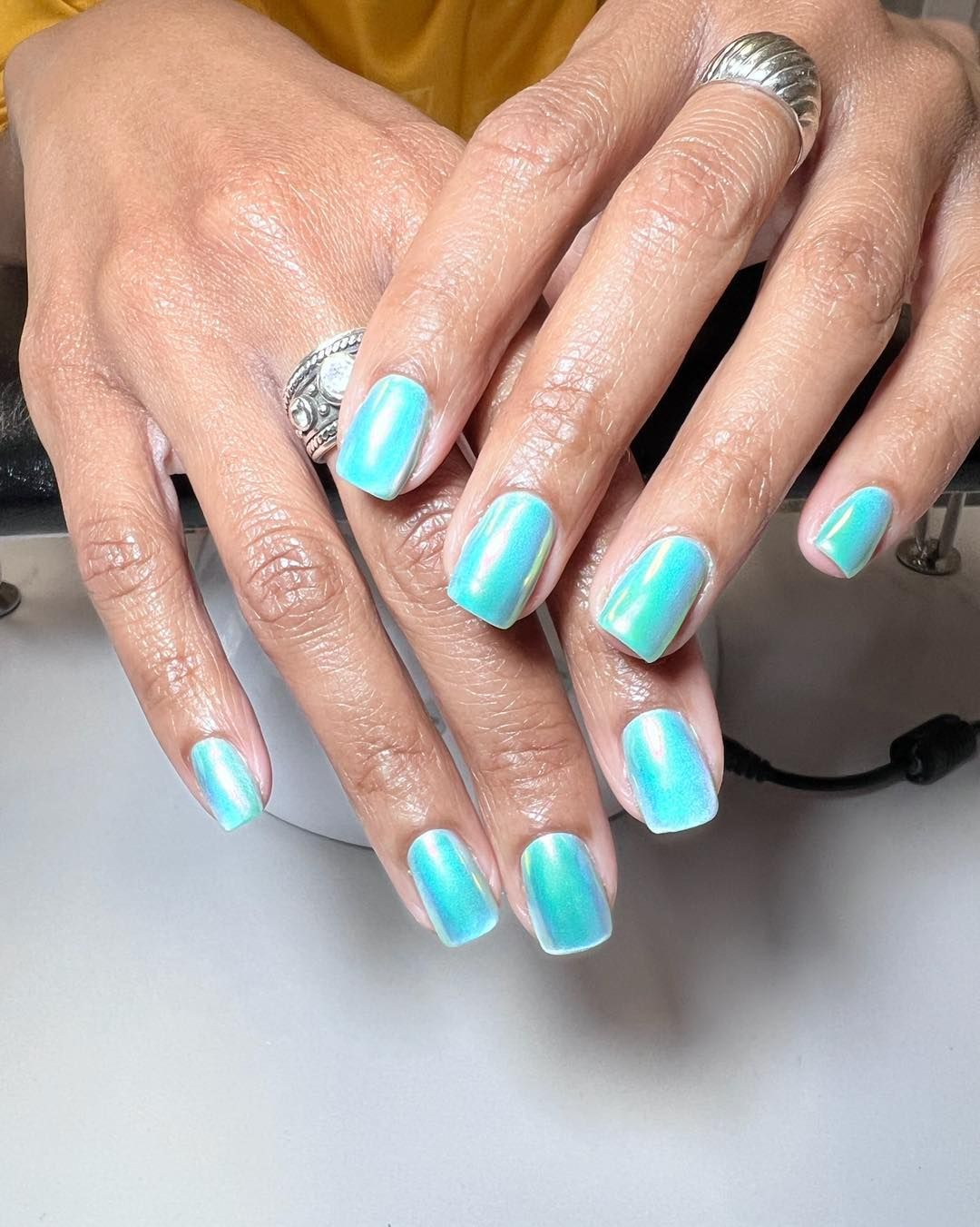 A woman 's hands with blue nails and a silver ring.