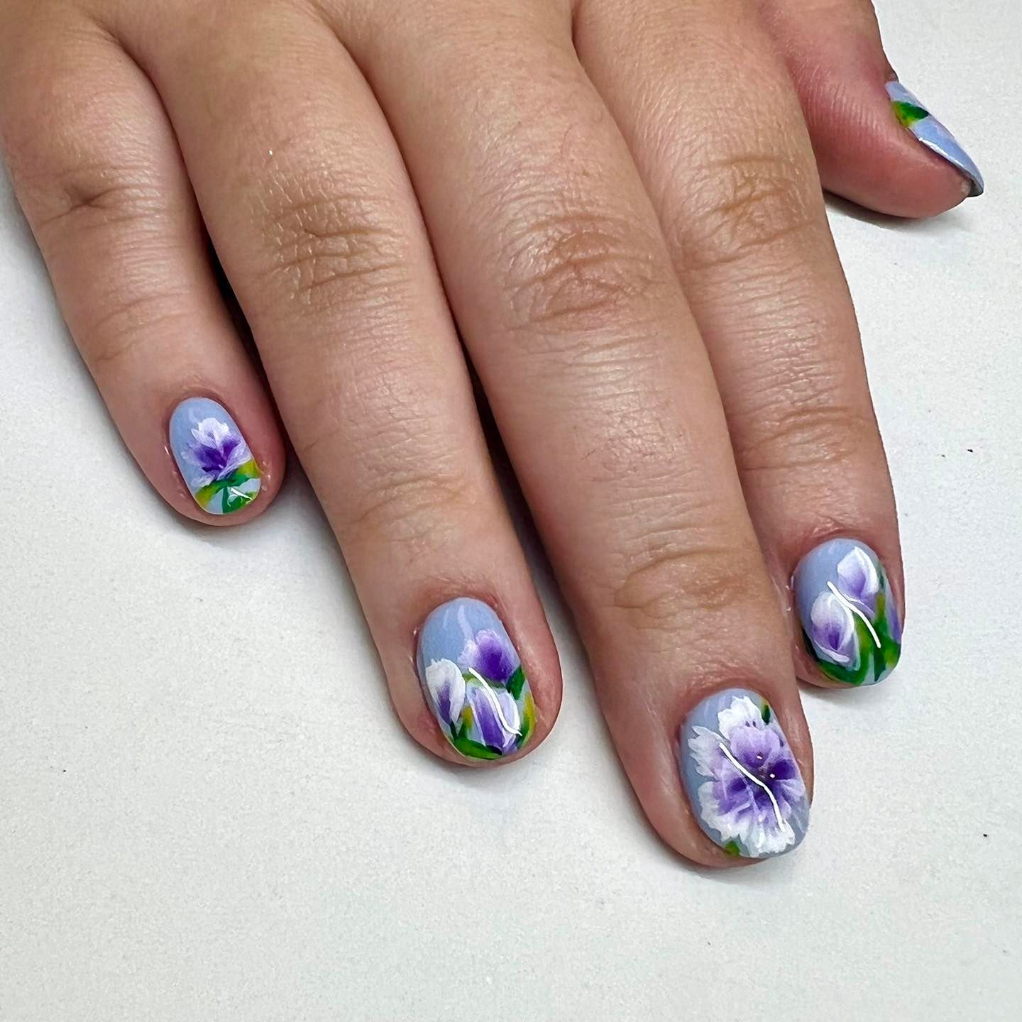 A woman 's nails are painted with purple and white flowers