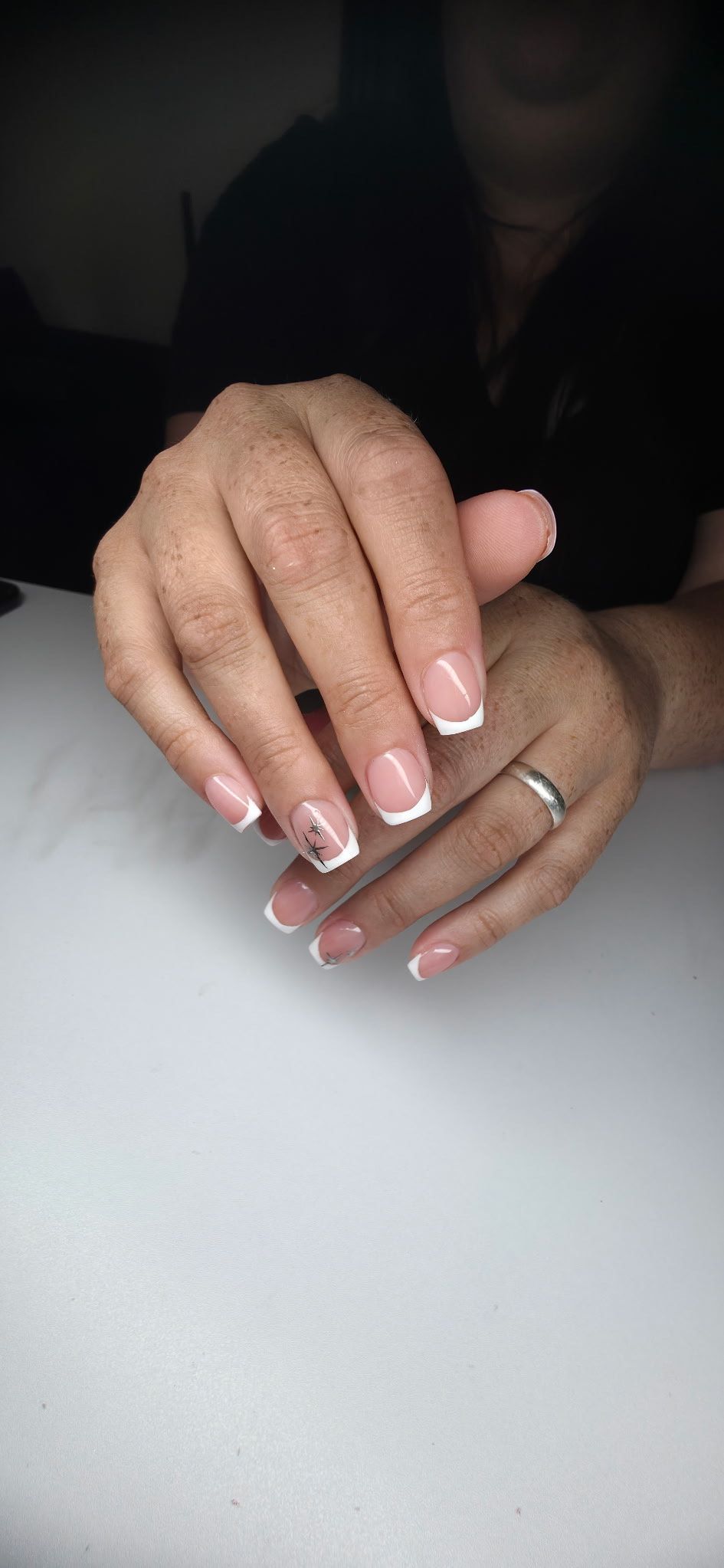 A close up of a woman 's hands with french manicure and a wedding ring.